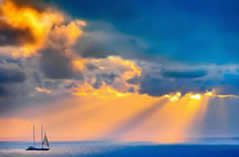 Image of sailboat out at sea with rays of light shining through dark clouds