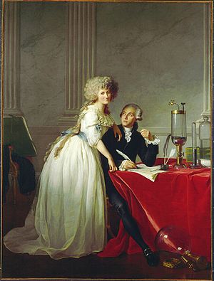 Woman in white dress leaning on man at table with notes and science equipment