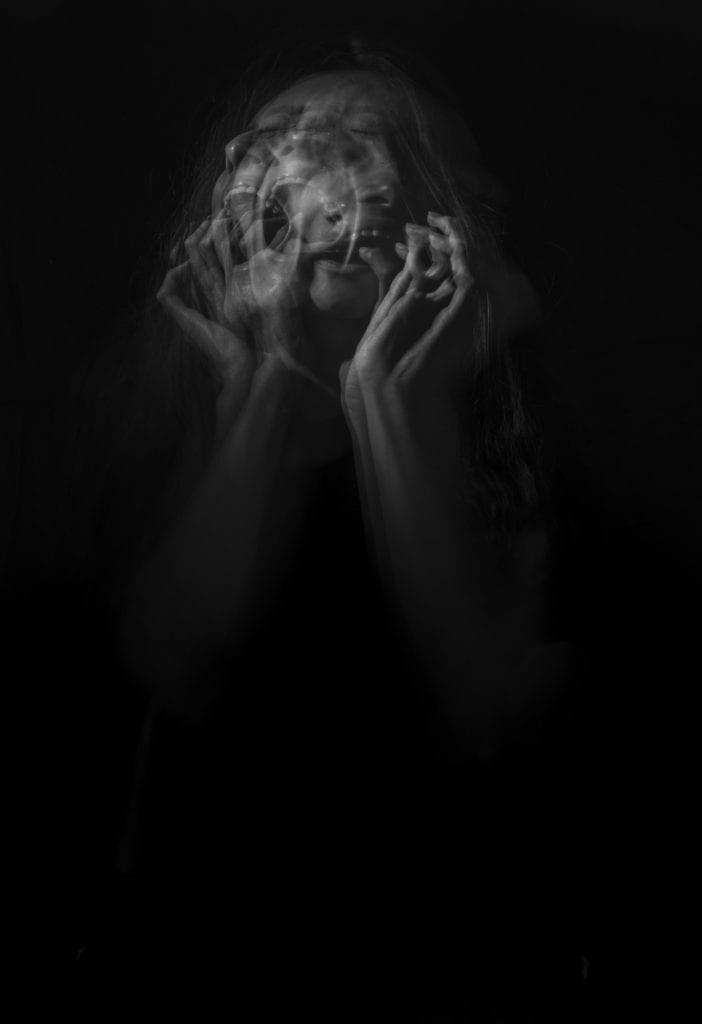 Photo by Camila Quintero Franco on Unsplash. A multilayered, black and white image of a frenzy woman scratching her face and screaming. 