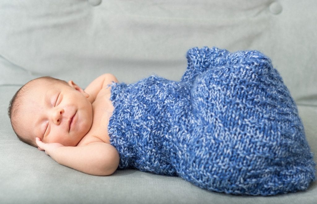 Photograph of a newborn in a blue blanket, like those born with the help of the Chicago Maternity Center