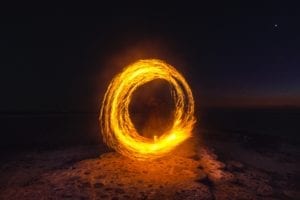 A fire dancer creates a burning circle of fire on a beach at night