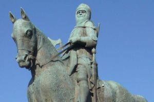 Robert the Bruce in battle armor on horseback. He is depicted wielding an axe and staring out into the distance, and the statue has gone green from oxidation.