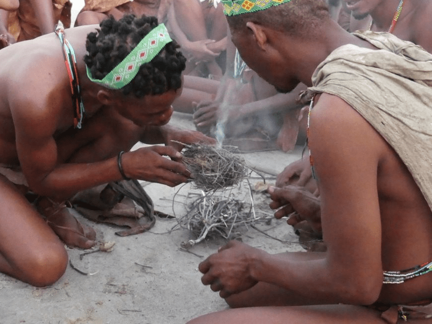 People wearing beads lighting a fire with twigs